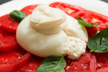 Delicious fresh cheese made from cream and milk - burrata. Italian tender cheese with tomato and greens salad close up
