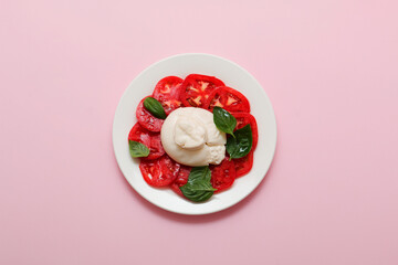 Delicious fresh cheese made from cream and milk - burrata. Italian tender cheese with tomato and greens salad on pink background