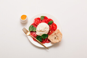 Delicious fresh cheese made from cream and milk - burrata. Italian tender cheese with tomato and greens salad, bread and olive oil.