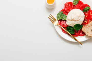 Delicious fresh cheese made from cream and milk - burrata. Italian tender cheese with tomato and greens salad, bread and olive oil.