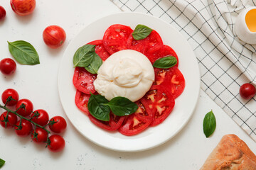 Delicious fresh cheese made from cream and milk - burrata. Italian tender cheese with tomato and greens salad, bread and olive oil.