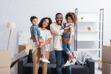 happy african american couple holding kids in hands in new apartment