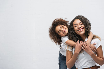 cheerful child embracing happy african american mother on grey