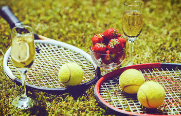 Tennis game. Strawberries, champagne and tennis balls with rackets on the green grass. Sport,...