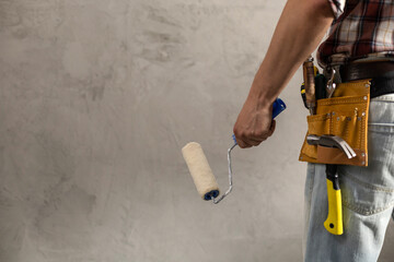 Construction worker man holding paint roller tool near wall. Male hand and construction tools