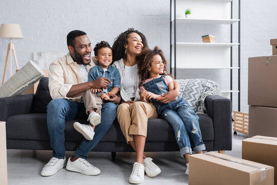 happy african american family looking away while sitting on couch in new apartment