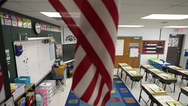 Slow boom down from US flag to reveal an empty school classroom during pandemic.