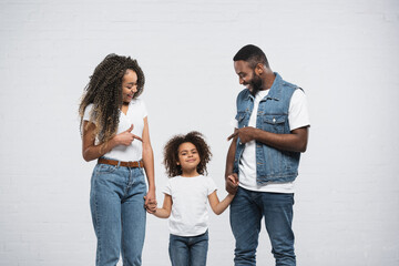 cheerful african american parents pointing at daughter on grey