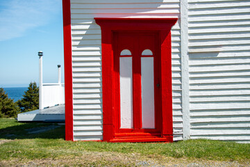 The exterior of a vintage white wooden building with vibrant red trim. There's an old wood door...