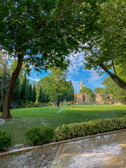 Beautiful view of cloudy sky and green tree in the park. Automatic sprinkler watering grass. Selective focus.