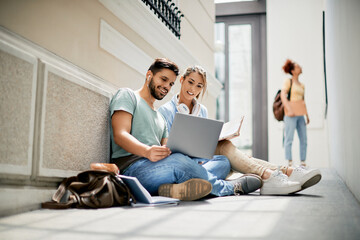 Happy university friends use laptop while studying in hallway.