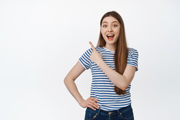 Image of happy young woman pointing at upper left corner, store product and smiling, showing announcement, sale info, standing over white background