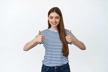 Smiling confident woman showing thumbs up and looking satisfied at camera, white background