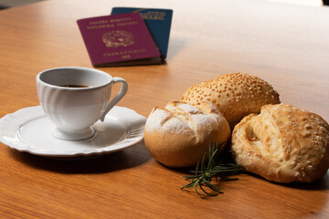 In the foreground, Italian and Brazilian passport, in the background and blurred a small cup of coffee and three loaves of bread with a sprig of rosemary decorating the scene.