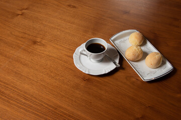 black coffee served in white cup and saucer, beside cheese bread in white rectangular plate on wooden table.