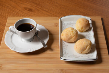 afternoon snack , coffee served in a small cup and saucer beside a silver spoon and three pieces of cheese served in a white dish