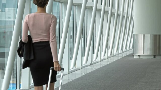 Back view of a business woman walking and carrying a suit case in an airport