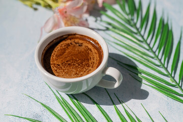 morning coffee americano in a cup of aromatic sunshine and shadows with a palm leaf