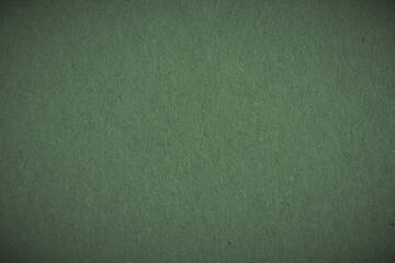 The surface of dark green cardboard. Paper texture with cellulose fibers. Paperboard wallpaper or background with vignetting. Modern, futuristic, elegant autumn color. Macro