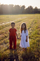 Naklejka na ściany i meble friend a boy in red clothes and a girl in a white dress walk through mown field at sunset in summer
