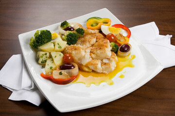 Posta de peixe com legumes em prato branco no fundo de mesa.