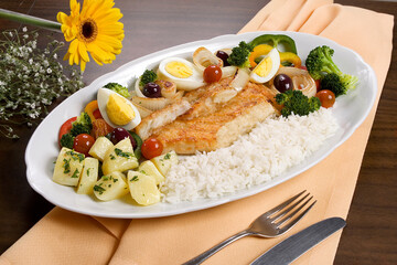 Delicioso prato com bacalhau e acompanhamento de arroz, batatas, ovos, azeitonas pretas, e legumes. no fundo de mesa decorada.
