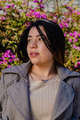 artistic portrait of a young hispanic latin woman looking away with pink flowers in the background. vertical photo