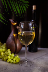 a glass of white wine with a grape bottle and a clay decanter