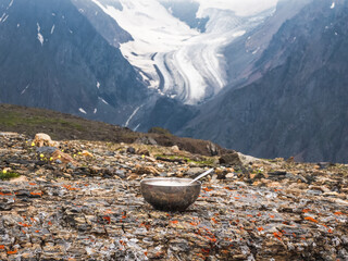 Tourist bowl with a spoon is laid out on a stone against the background of a glacier and high mountains. Lunch time, high-altitude trekking.
