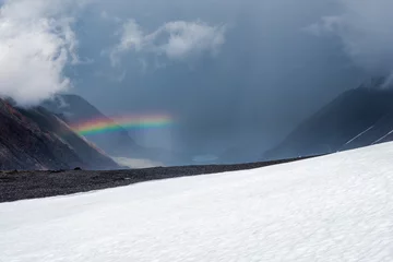Fotobehang Rainbow over a winter snow mountain valley. Atmospheric alpine landscape with snowy mountains with rainbow in rainy and sunny weather. © sablinstanislav