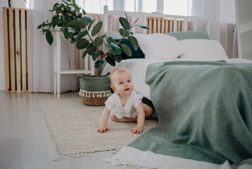 a baby girl in a muslin jumpsuit crawls on the floor in the bedroom - obrazy, fototapety, plakaty
