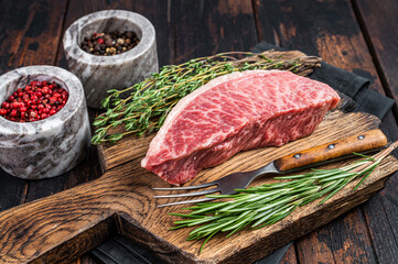 Wagyu A5 raw rump or sirloin steak, kobe beef meat on a butchery board. Dark wooden background. Top...
