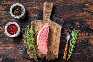 Wagyu A5 raw rump or sirloin steak, kobe beef meat on a butchery board. Dark wooden background. Top view - obrazy, fototapety, plakaty