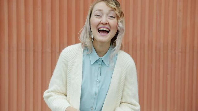Portrait of joyful blond woman laughing hard standing outdoors and looking at camera enjoying positive emotions. People and happiness concept.