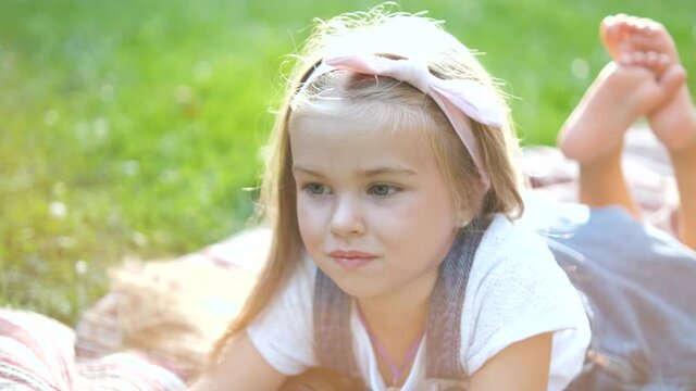 Portrait of pretty child girl resting outdoors in summer park.