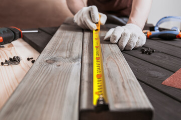 Exact measured. Close up of young male carpenter in gloves making measurements on the wooden plank...