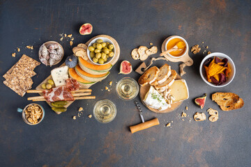 Snacks table with Italian snacks and wine in glasses. Brushetta, a kind of cheese board on a black background. Top view, flat layer - obrazy, fototapety, plakaty