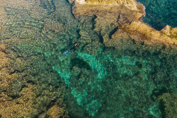Aerial drone bird's eye view of swimming spearfishing diver in rocky seascape located in Costa Blanca, Torrevieja, Spain