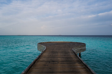 Fototapeta premium Wooden bridge or pier on tropical white sand beach with clear blue ocean and sky on sunny day. Boardwalk into the ocean and turquoise water. Summer holidays background with copy space. Crossroads Mald