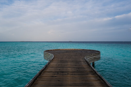 Wooden bridge or pier on tropical white sand beach with clear blue ocean and sky on sunny day. Boardwalk into the ocean and turquoise water. Summer holidays background with copy space. Crossroads Mald