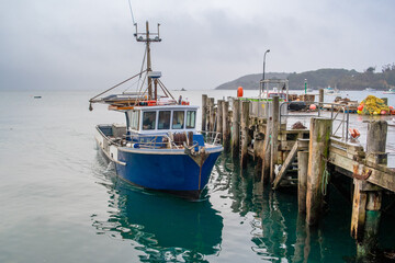 A fishing boat docked at the wharf, floats on the still sea, waiting for the next trip out on the...