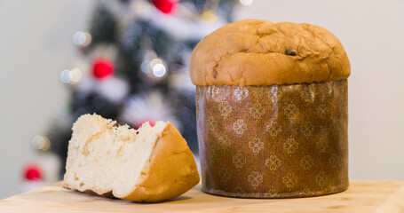 Panettone slice with Christmas tree
and blurry lights flashing in the background. Panettone concept. Christmas concept.