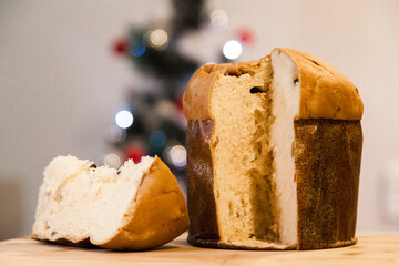 Panettone slice with Christmas tree
and blurry lights flashing in the background. Panettone concept. Christmas concept.