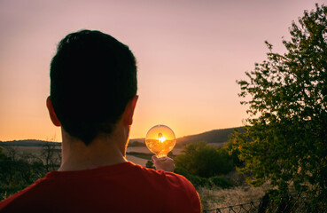 Man holding a light bulb during a sunset - obrazy, fototapety, plakaty