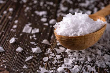 Healthy sea salt in crystals on wooden spoon closeup. Close up Low key composition on dark rustic wooden background. Selective focus.