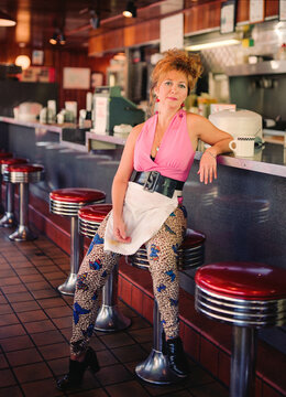 Portrait of waitress with big hair at old school diner sitting on bar stool 