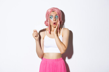Image of excited silly girl in pink anime wig and bright makeup, looking amazed at credit card,...