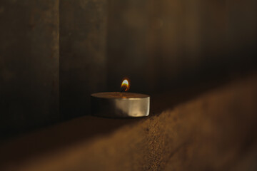 Tea light candle with wick burning with small flame in dark and moody setting