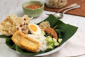 Nasi Pecel. Traditional Javanese Rice Dish of Steamed Rice with Vegetable Salad, Peanut Sauce Dressing, Tempeh, Tofu Beancurd, and Peyek Crackers. Pecel Madiun is Most Popular Variant