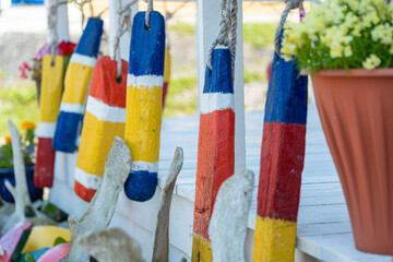 Multiple antique wooden lobster fishing buoys hanging on a light colored wooden panel wall. The colorful, worn, and textured wooden markers are strung together with old fishing rope.